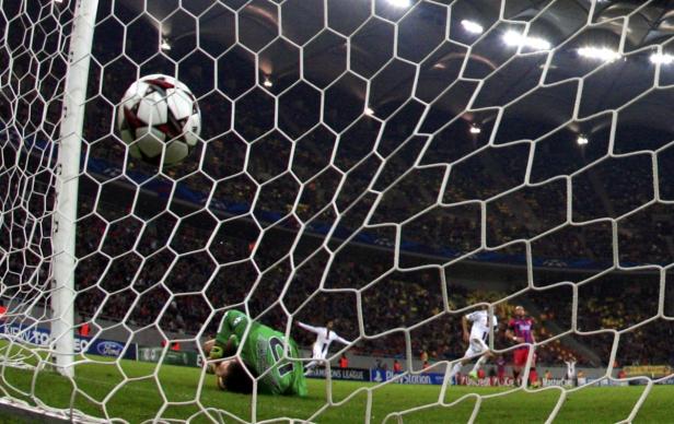 Ein Fußball fliegt ins Netz, während der Torwart am Boden liegt.