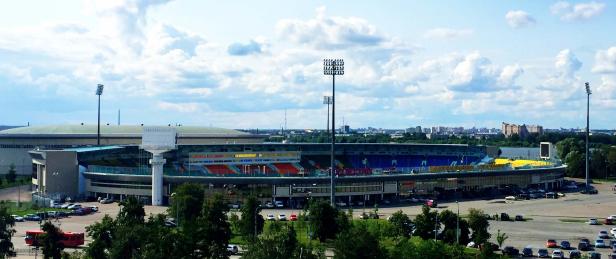 Ein Panoramablick auf ein Stadion mit Parkplatz und umliegender Stadtlandschaft.