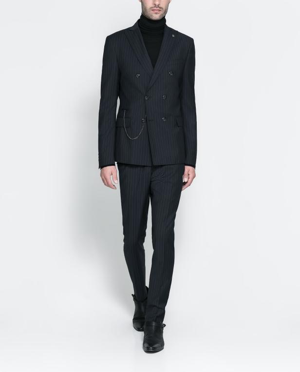 Ein Mann in einem dunkel gestreiften Anzug und Rollkragenpullover posiert vor einem weißen Hintergrund.