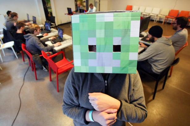 Eine Person mit einer Creeper-Maske aus „Minecraft“ vor einer Gruppe von Leuten an Computern.