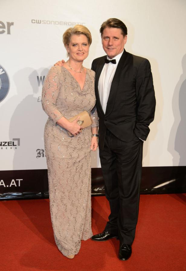 Ein Mann im Smoking und eine Frau im Abendkleid posieren auf einem roten Teppich.