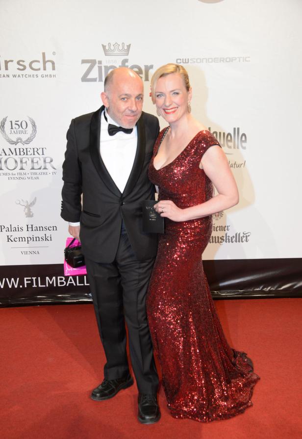 Ein Mann im Smoking und eine Frau in einem roten Paillettenkleid posieren auf dem roten Teppich.