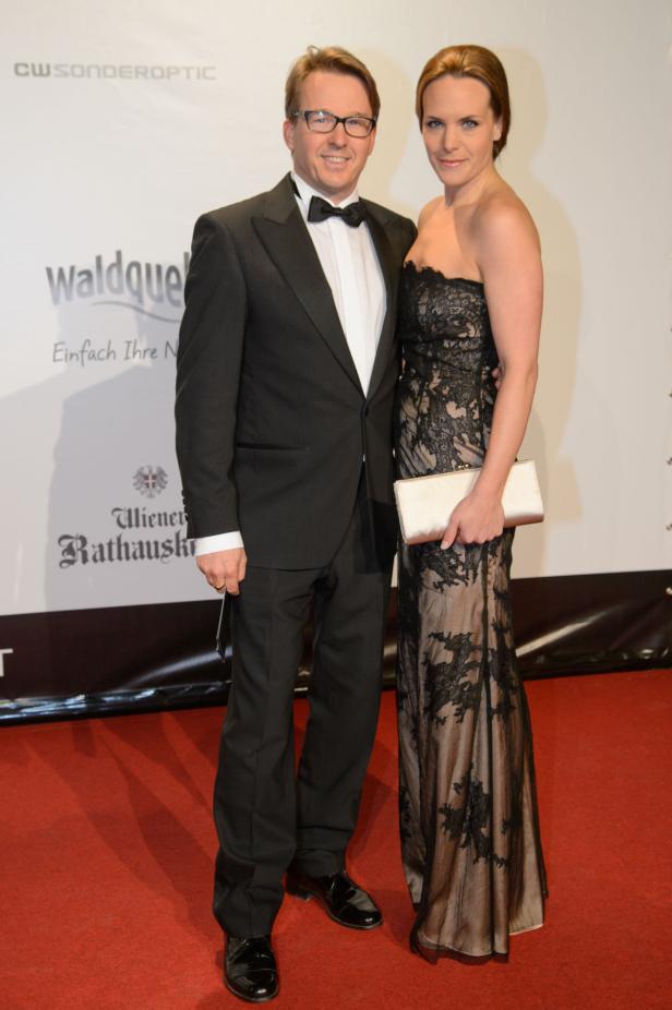Ein Mann im Smoking und eine Frau im Abendkleid posieren auf einem roten Teppich.