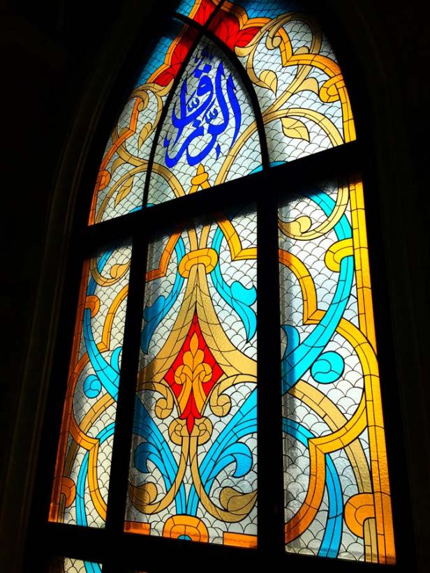 Ein buntes Glasfenster mit arabischer Schrift und floralen Mustern.