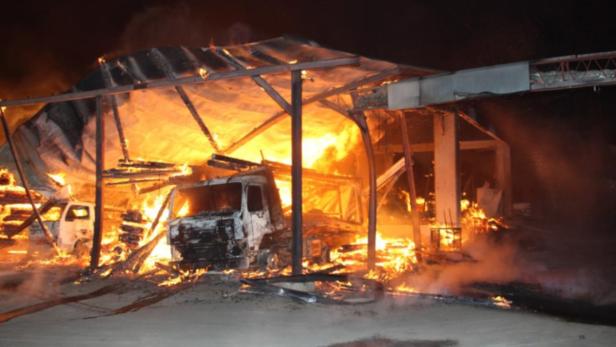 Ein Gebäude und mehrere Lastwagen stehen in Flammen.