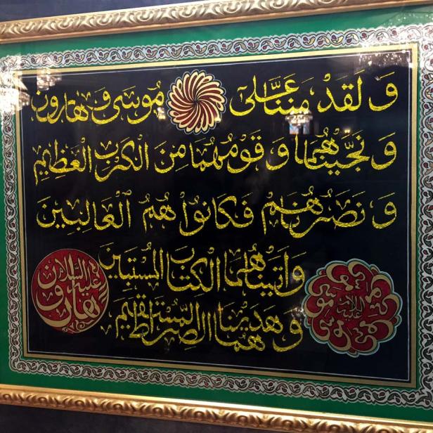 Gerahmtes Kunstwerk mit goldener arabischer Kalligraphie auf schwarzem Grund.