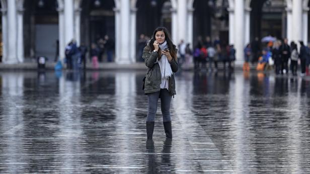 Eine Frau steht auf dem überfluteten Markusplatz in Venedig und telefoniert.