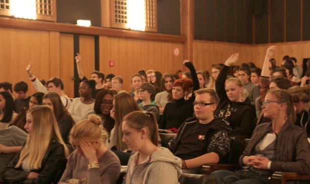Viele Studenten sitzen in einem Hörsaal, einige haben ihre Hände gehoben.
