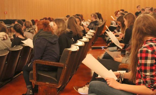 Viele Menschen sitzen in einem Auditorium und halten Papier in den Händen.