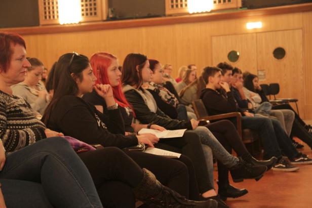 Eine Gruppe von Menschen sitzt in einem Auditorium und hört aufmerksam zu.