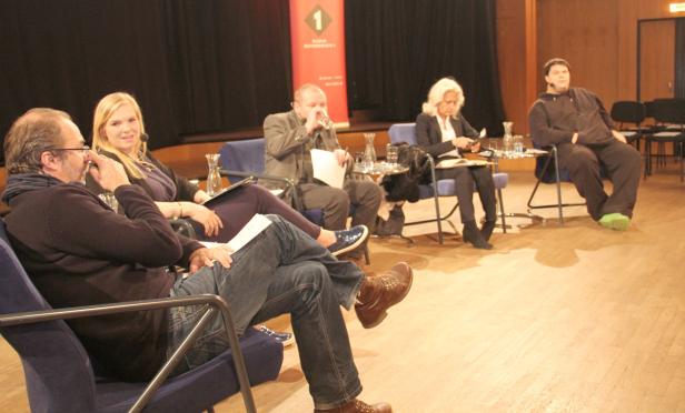 Fünf Personen sitzen auf einer Bühne während einer Podiumsdiskussion.