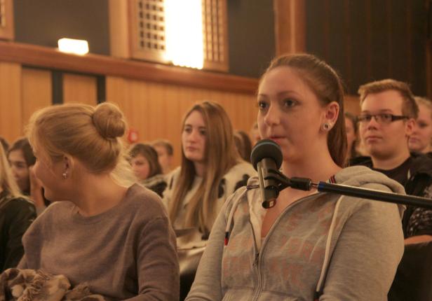Eine junge Frau spricht bei einer Veranstaltung in ein Mikrofon.