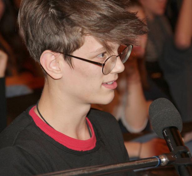 Ein junger Mann mit Brille spricht in ein Mikrofon.