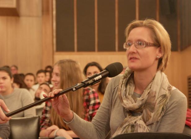 Eine Frau mit Brille spricht in ein Mikrofon vor einem Publikum.