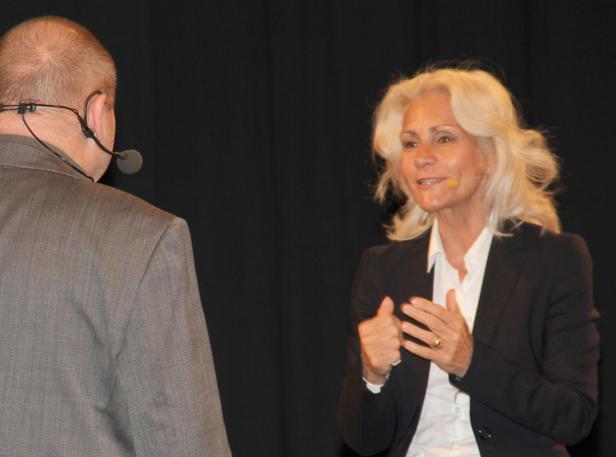 Eine Frau mit blonden Haaren spricht vor einem Publikum.