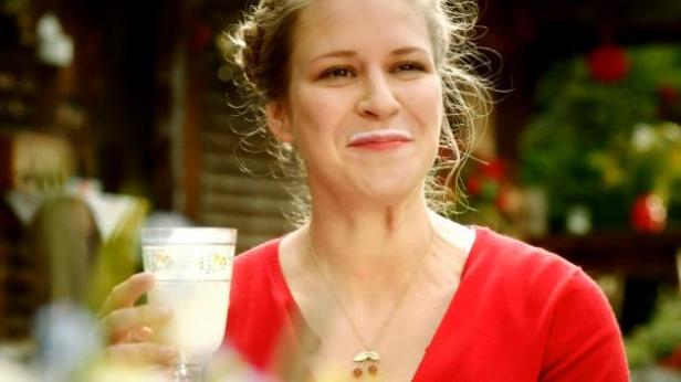 Eine Frau mit Milchbart hält ein Glas Milch in der Hand.
