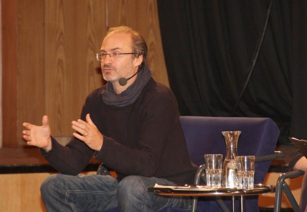 Ein Mann mit Brille und Mikrofon gestikuliert während einer Präsentation.