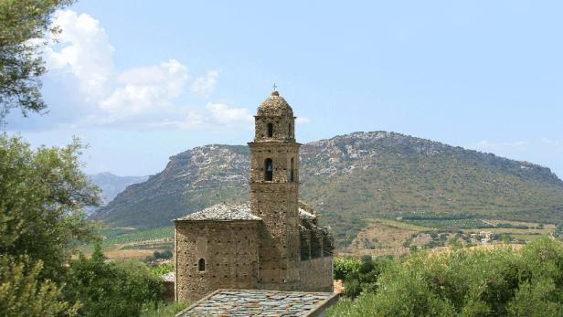 Eine alte Steinkirche mit einem Glockenturm in einer hügeligen Landschaft.