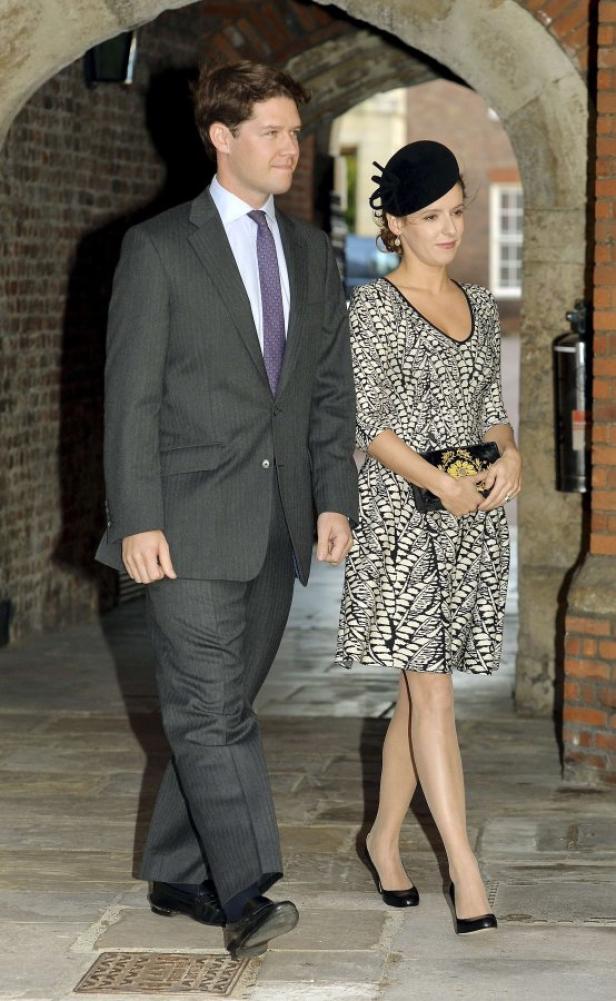 Ein Mann im Anzug und eine Frau mit Hut verlassen ein Gebäude.