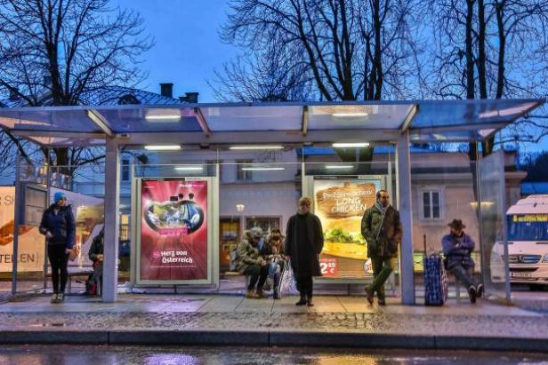 (c: epamedia) Menschen warten an einer Bushaltestelle mit Werbeplakaten.