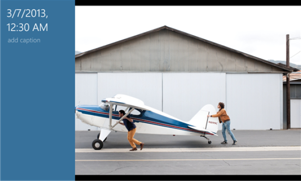 Zwei Männer schieben ein kleines blau-weißes Flugzeug vor einem Hangar.