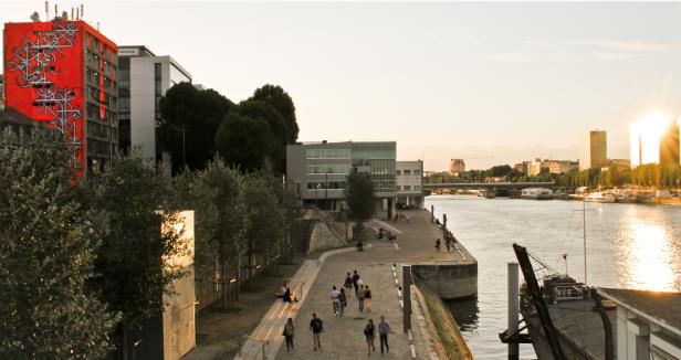 Blick auf die Seine in Paris mit Passanten und einem Gebäude mit Graffiti.