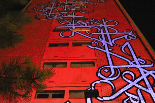 Ein rotes Gebäude ist mit blauer Kalligrafie beleuchtet.