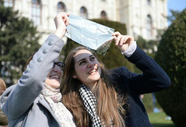 Zwei junge Frauen halten eine reflektierende Folie in die Sonne.