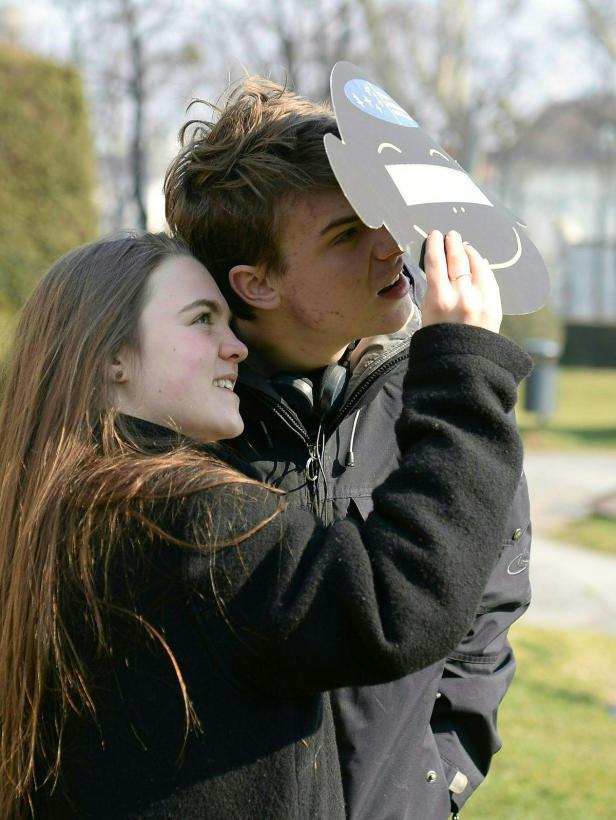 Ein junges Paar betrachtet mit einer Pappmaske die Sonne.