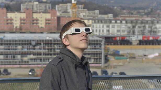 Ein junger Mann mit einer Sonnenfinsternisbrille blickt in den Himmel.