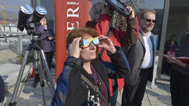 Eine Gruppe von Menschen beobachtet eine Sonnenfinsternis mit speziellen Brillen und einem Teleskop.
