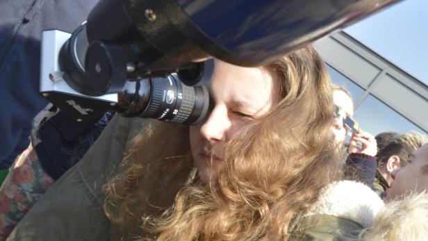 Ein Mädchen blickt durch ein Teleskop in den Himmel.