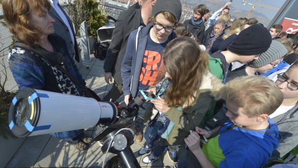 Eine Gruppe von Menschen steht um ein Teleskop auf einer Dachterrasse.