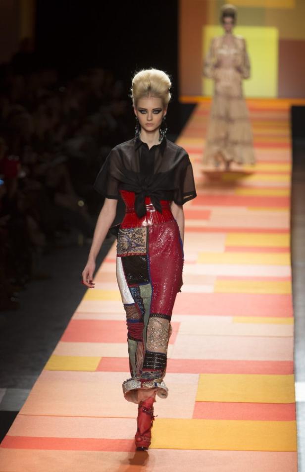 Ein Model mit auffälligem Make-up präsentiert ein Patchwork-Outfit auf dem Laufsteg.