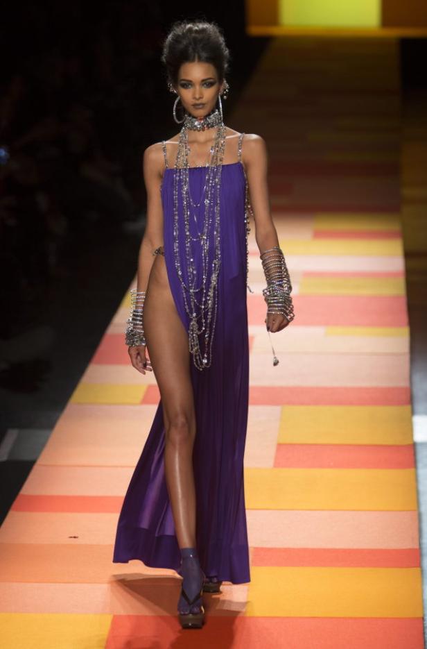 Ein Model in einem violetten Kleid mit hohem Schlitz auf einem Laufsteg.