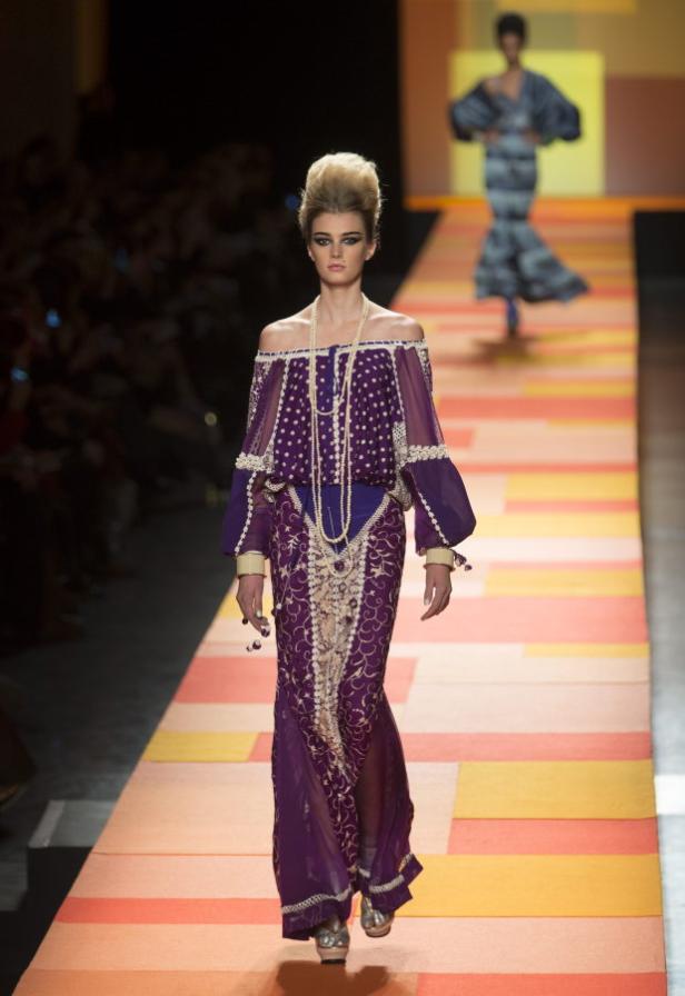 Eine Frau in einem lila, schulterfreien Kleid auf einem Laufsteg.