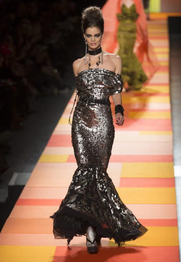 Ein Model präsentiert ein silbernes, schulterfreies Abendkleid auf einem Laufsteg.