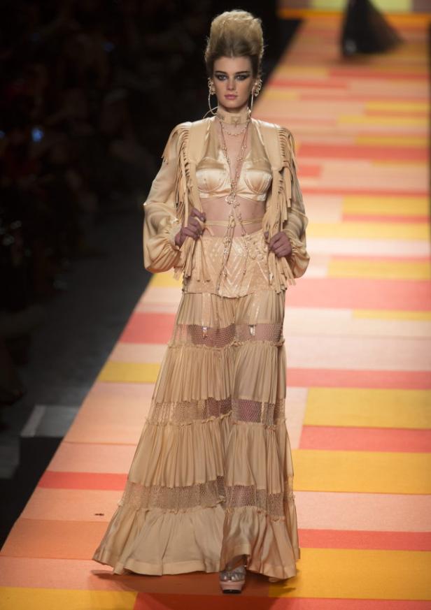 Ein Model präsentiert ein beiges Ensemble mit Fransen auf einem Laufsteg.