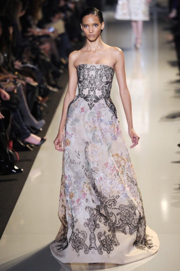 Ein Model präsentiert ein trägerloses, blumengemustertes Abendkleid auf dem Laufsteg.