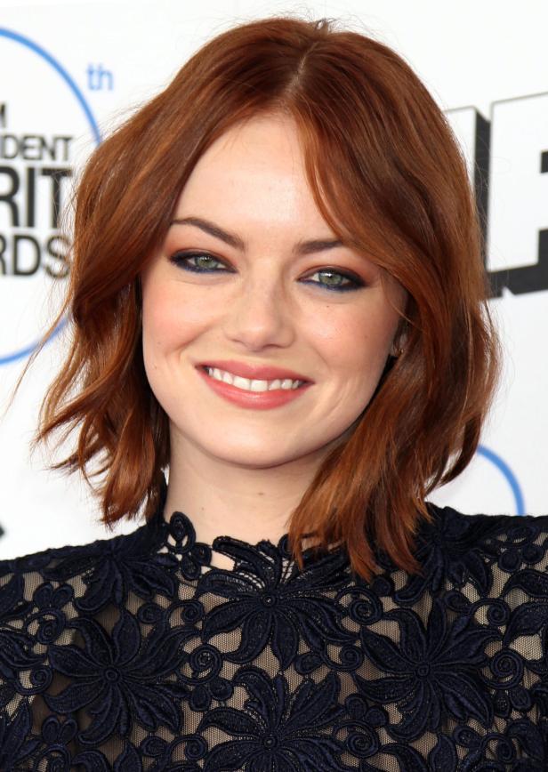 Emma Stone lächelt in einem Kleid mit floraler Spitze.