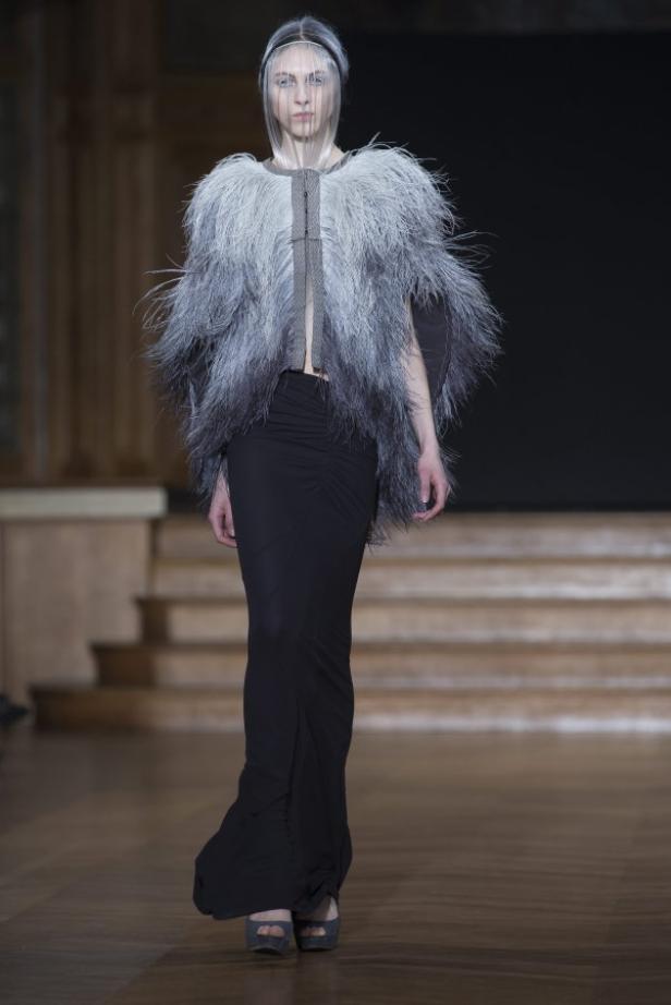 Eine Frau auf dem Laufsteg trägt ein extravagantes Outfit mit Federn und Schleier.