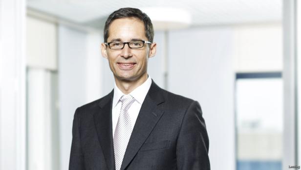 Ein Mann mit Brille und Anzug lächelt in die Kamera.