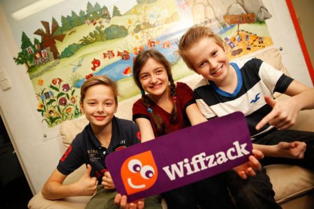 Drei Kinder sitzen auf einer Couch und halten ein Schild mit der Aufschrift „Wiffzack“.