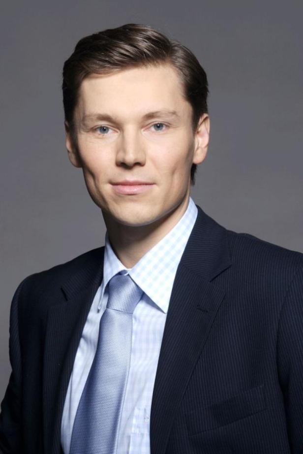 Ein Mann mit Anzug und Krawatte vor einem grauen Hintergrund.