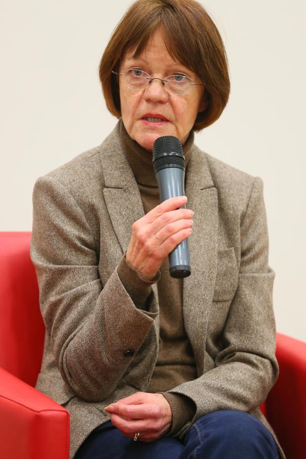 Eine Frau mit Brille spricht in ein Mikrofon, während sie in einem roten Sessel sitzt.
