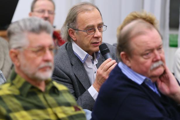 Ein Mann mit Brille spricht in ein Mikrofon vor Publikum.