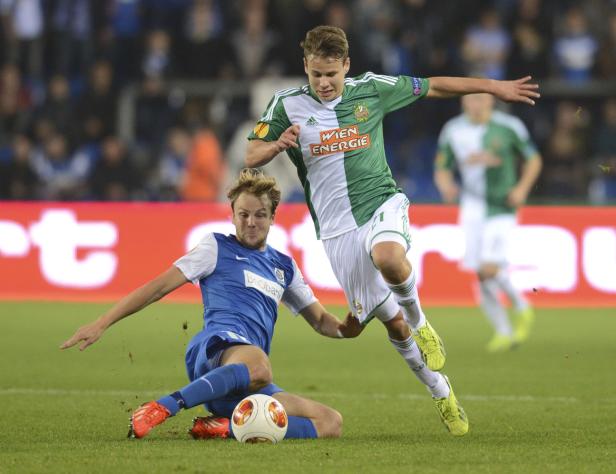 Ein Fußballspieler grätscht, während ein anderer über ihn springt.