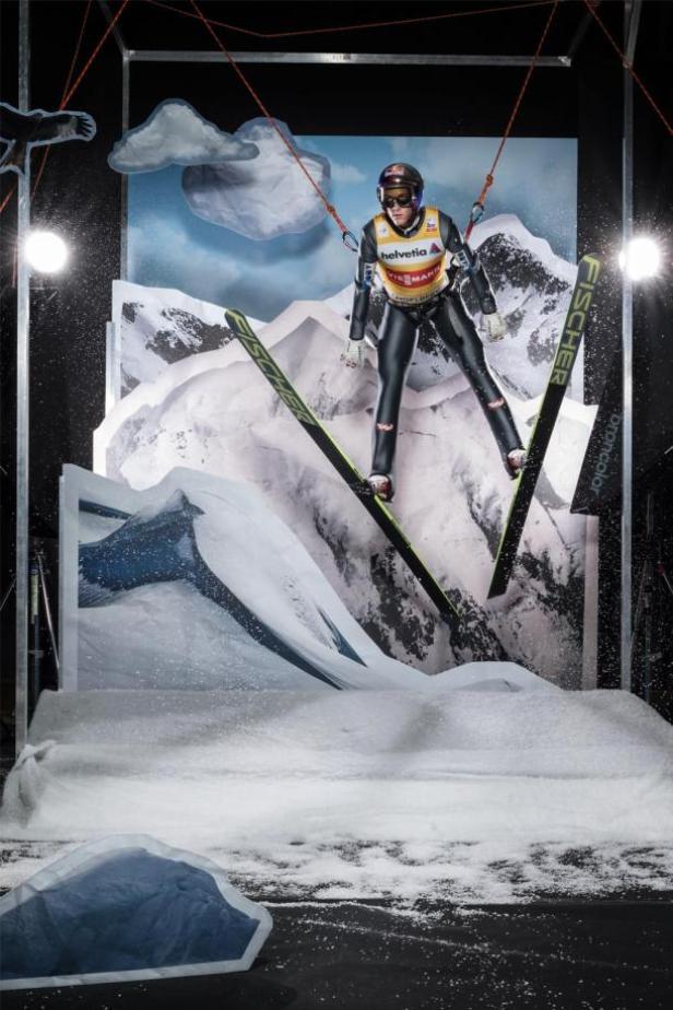 Schlierenzauer ausnahmsweise mit Seilsicherung. Wegen der Studio-Gefahren! Vielleicht? (c: zoom.at - markus berger) Eine Skispringerin in der Luft vor einer gemalten Bergkulisse.