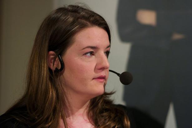 Eine Frau spricht mit einem Mikrofon vor einem dunklen Hintergrund.