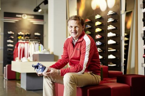Björn Gulden, CEO Puma: Ein Mann sitzt in einem Schuhgeschäft und hält einen blauen Kinderschuh in den Händen.
